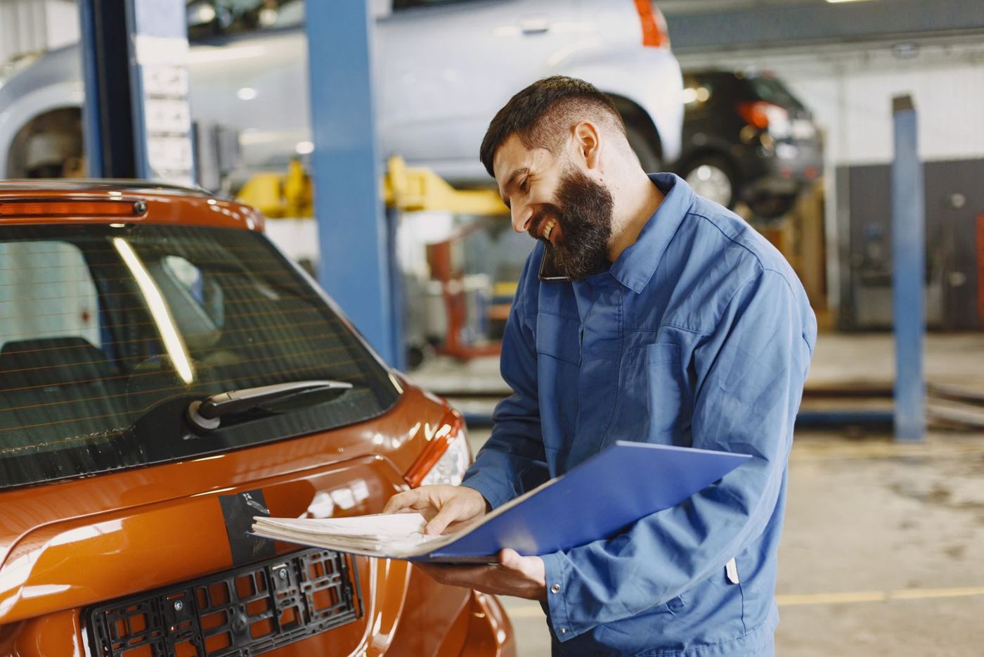 A smiling mechanic in coveralls taking a phone call in his shop (stock photo)